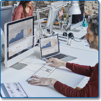  A male in an office sitting in front of an iMac and a MacBook, with both showing same contents on the screens  